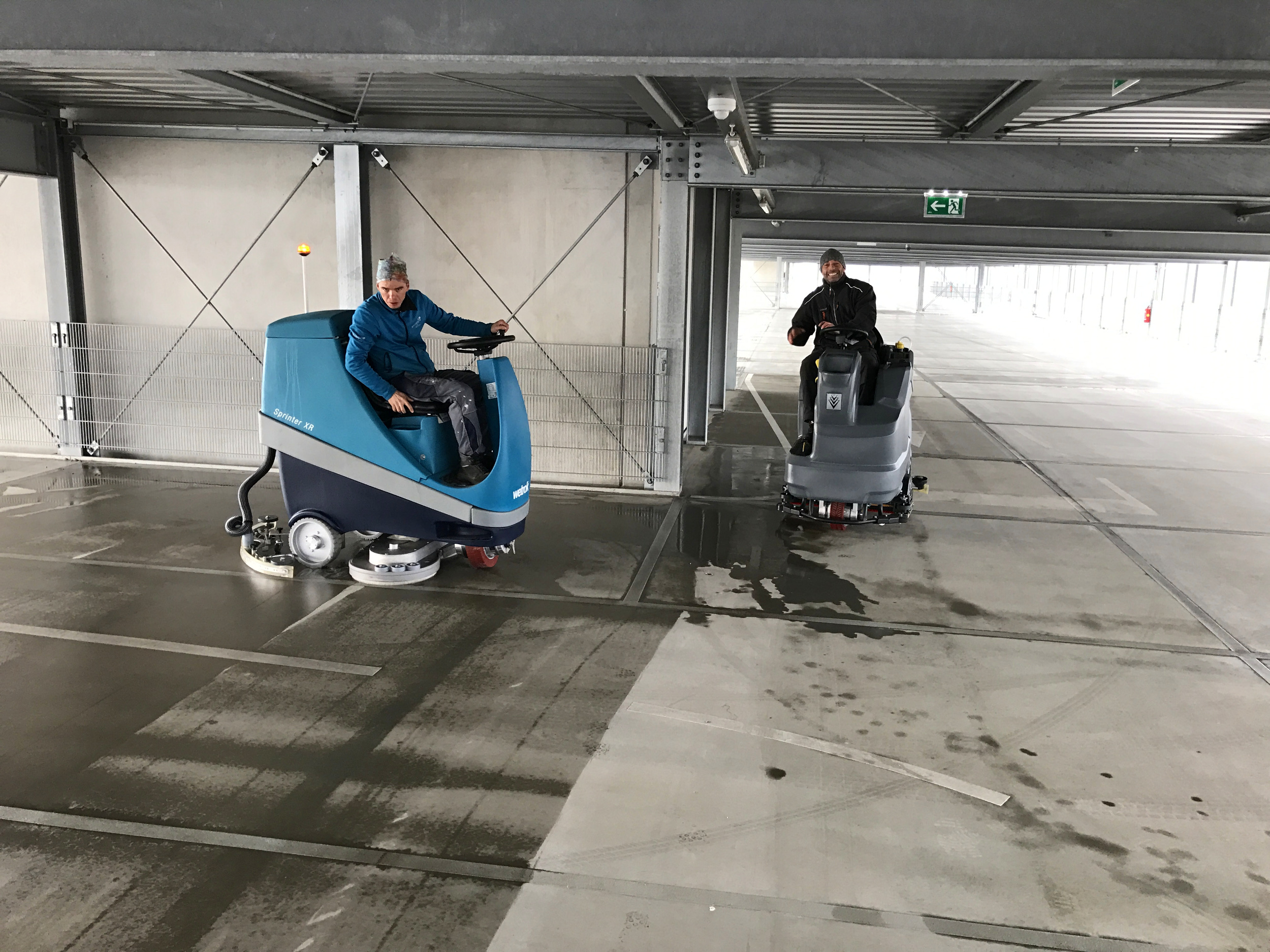 Zwei Reinigungsmaschinen in einer Tiefgarage während der Reinigung des Fußbodens.