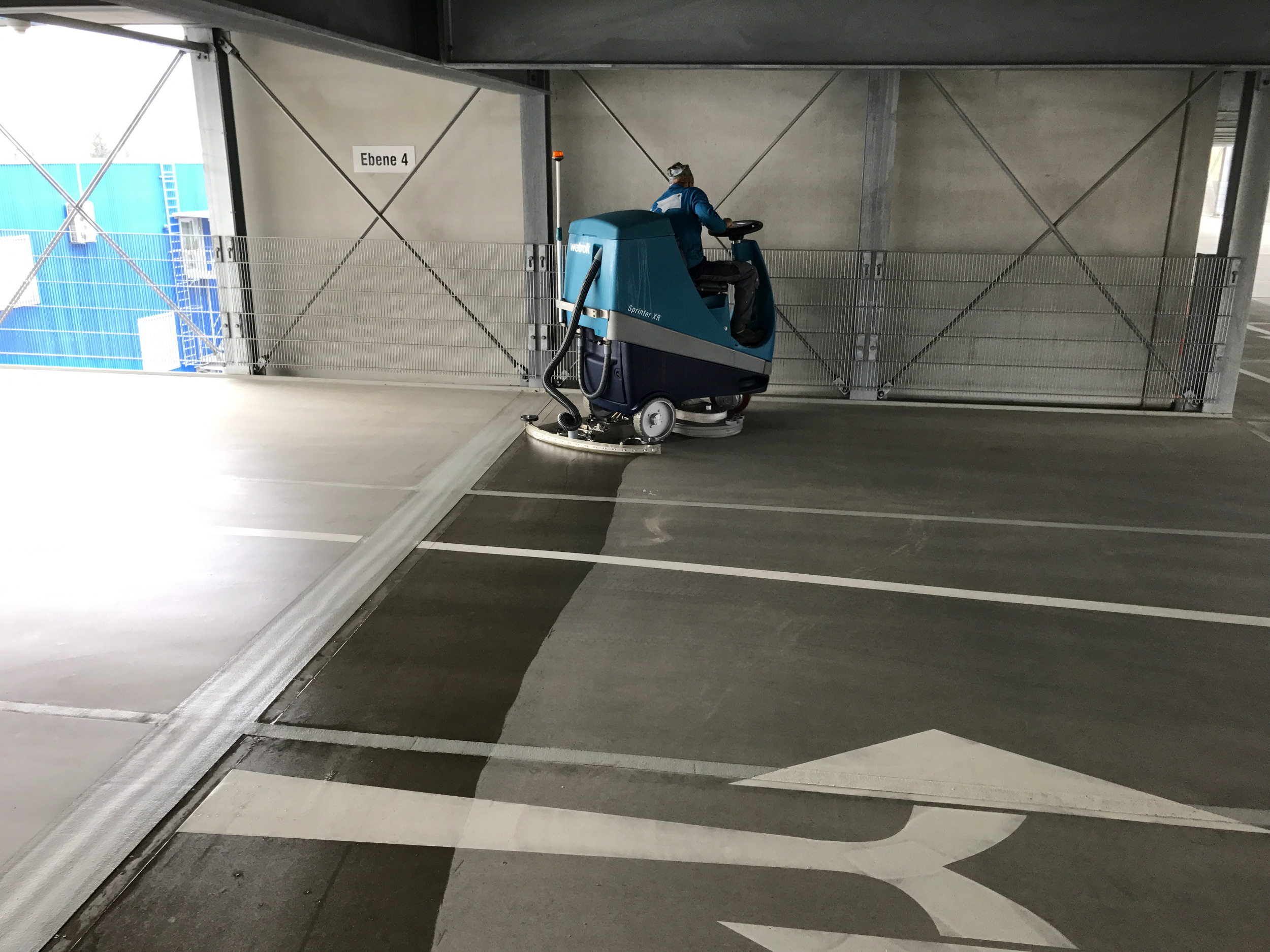 Eine Reinigungsmaschine reinigt den Boden in einer Tiefgarage mit einem klaren Blick auf die Fahrbahnmarkierungen.
