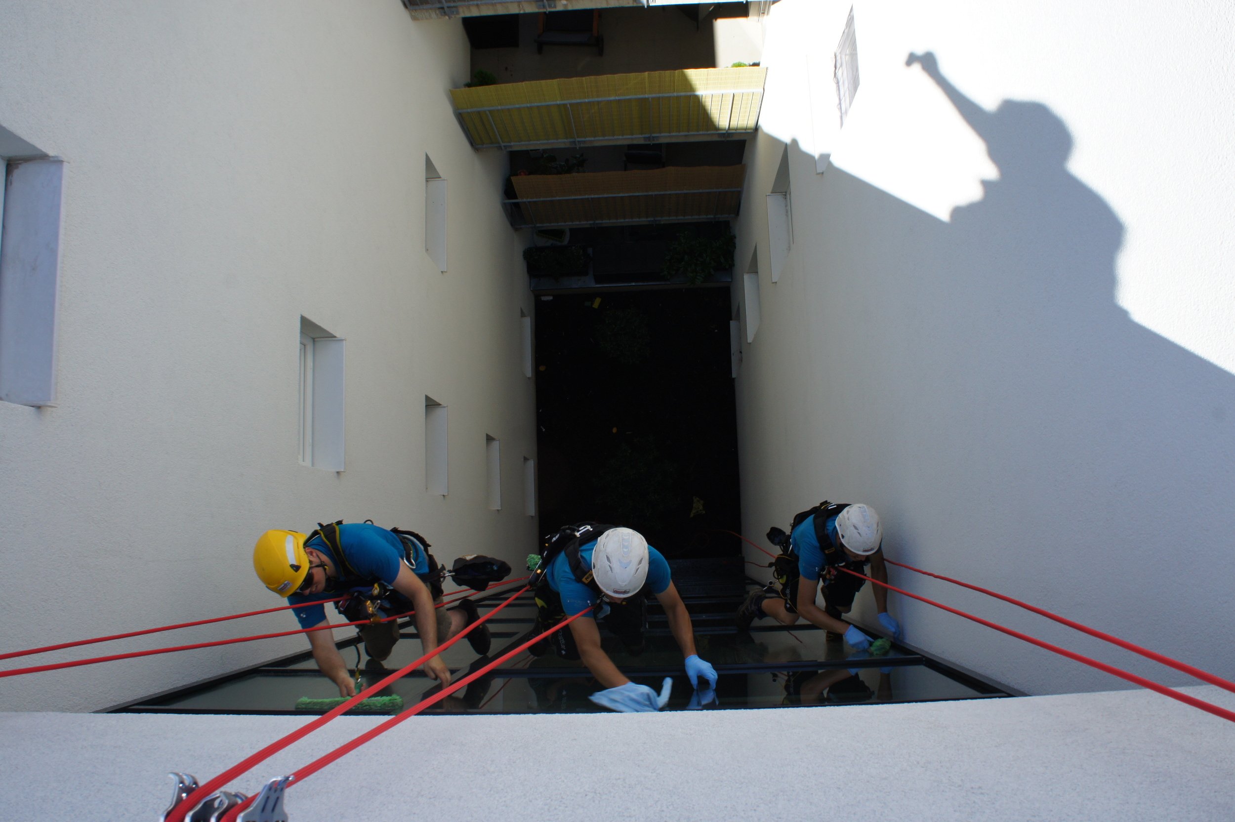 Drei Personen reinigen Fenster an einer Gebäudefassade mit Seilzugangstechnik.