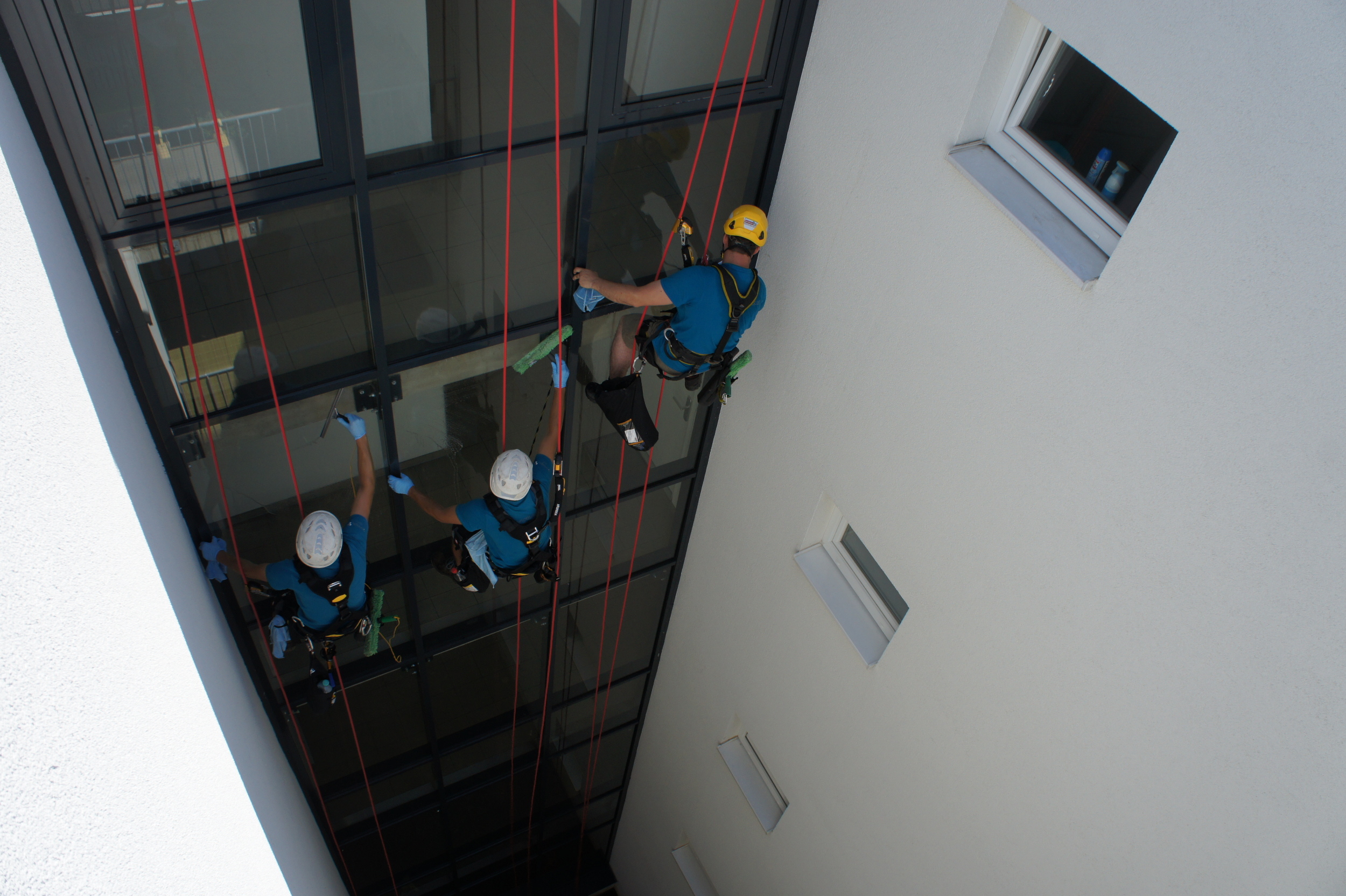 Zwei Fensterreiniger, die an einem Gebäude mit Seilzugangstechnik arbeiten.