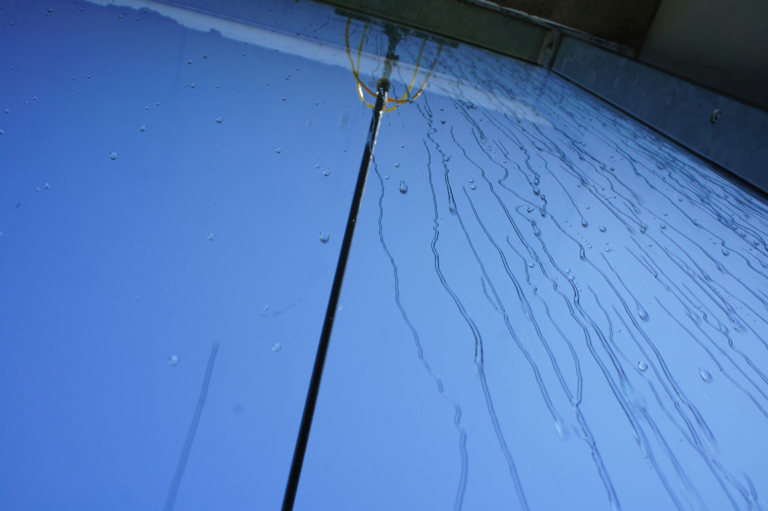 Wassertropfen, die an einer vertikalen Glasoberfläche herunterlaufen.