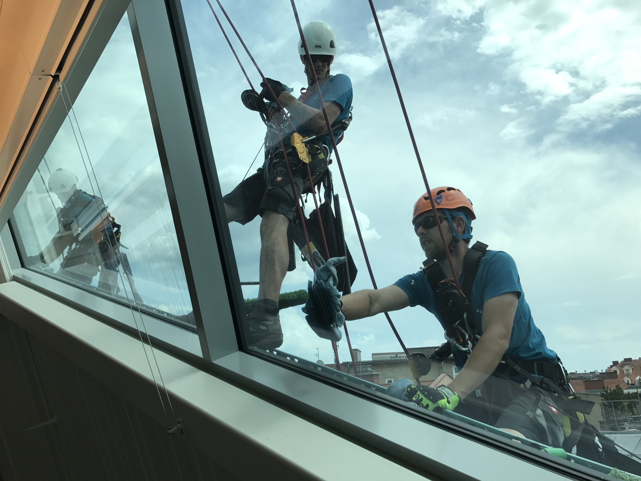 Zwei Industriekletterer reinigen eine große Fensterfläche an einem Gebäude mit Seiltechnik.