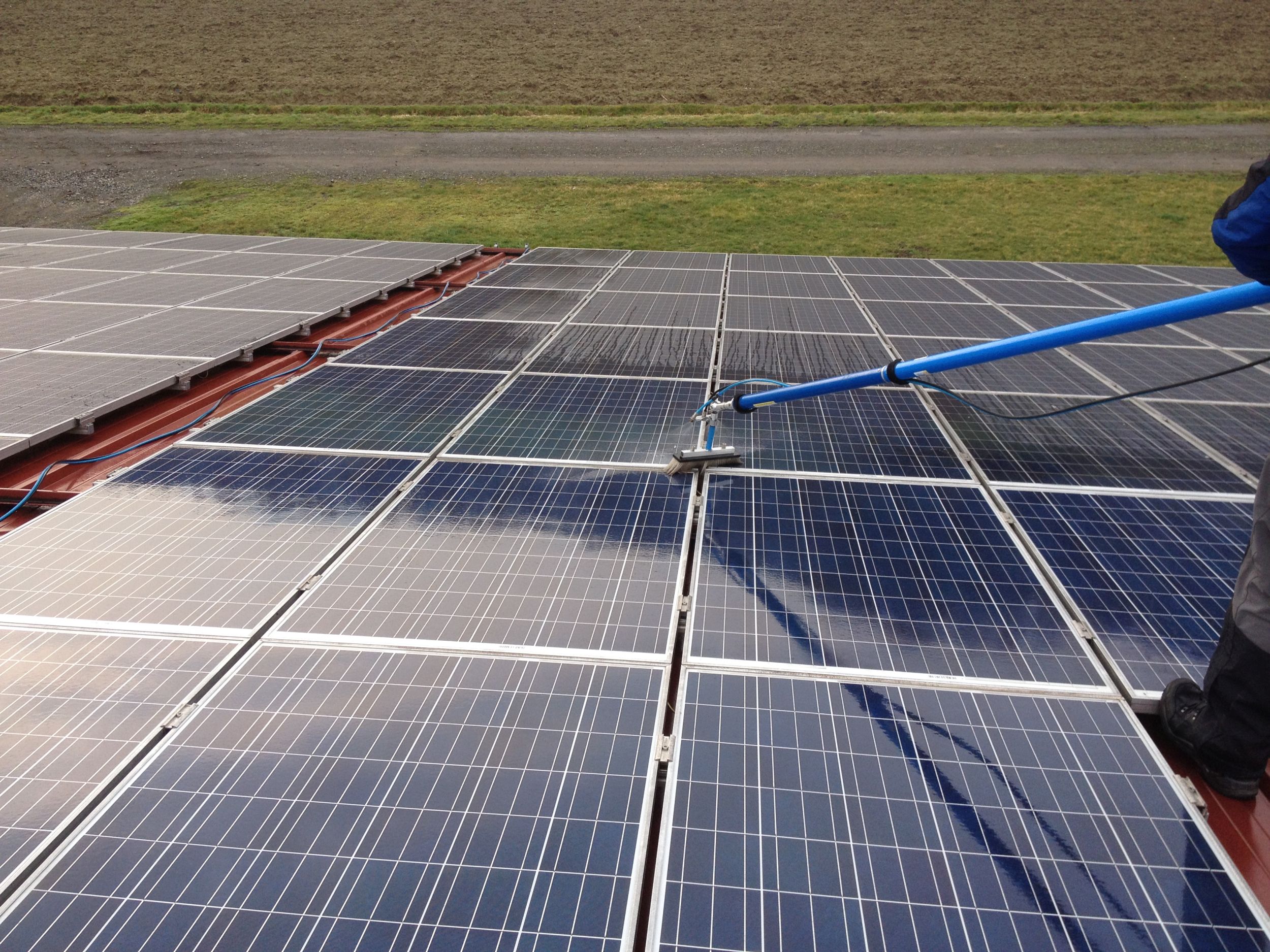 Person reinigt Solarpanels auf einem Dach mit einem langen Besen.