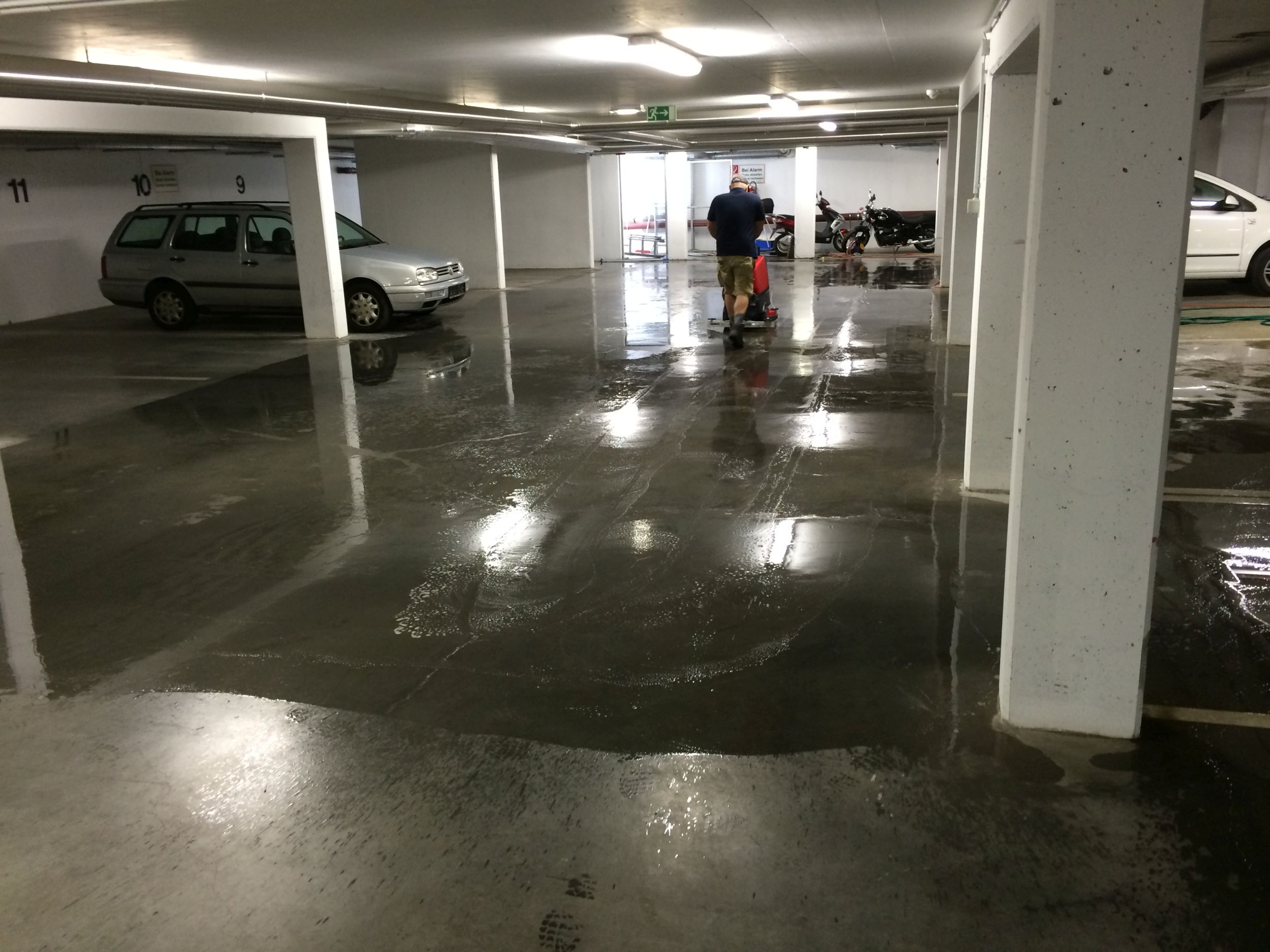 Mann reinigt den Boden einer Tiefgarage mit einer Reinigungsmaschine.