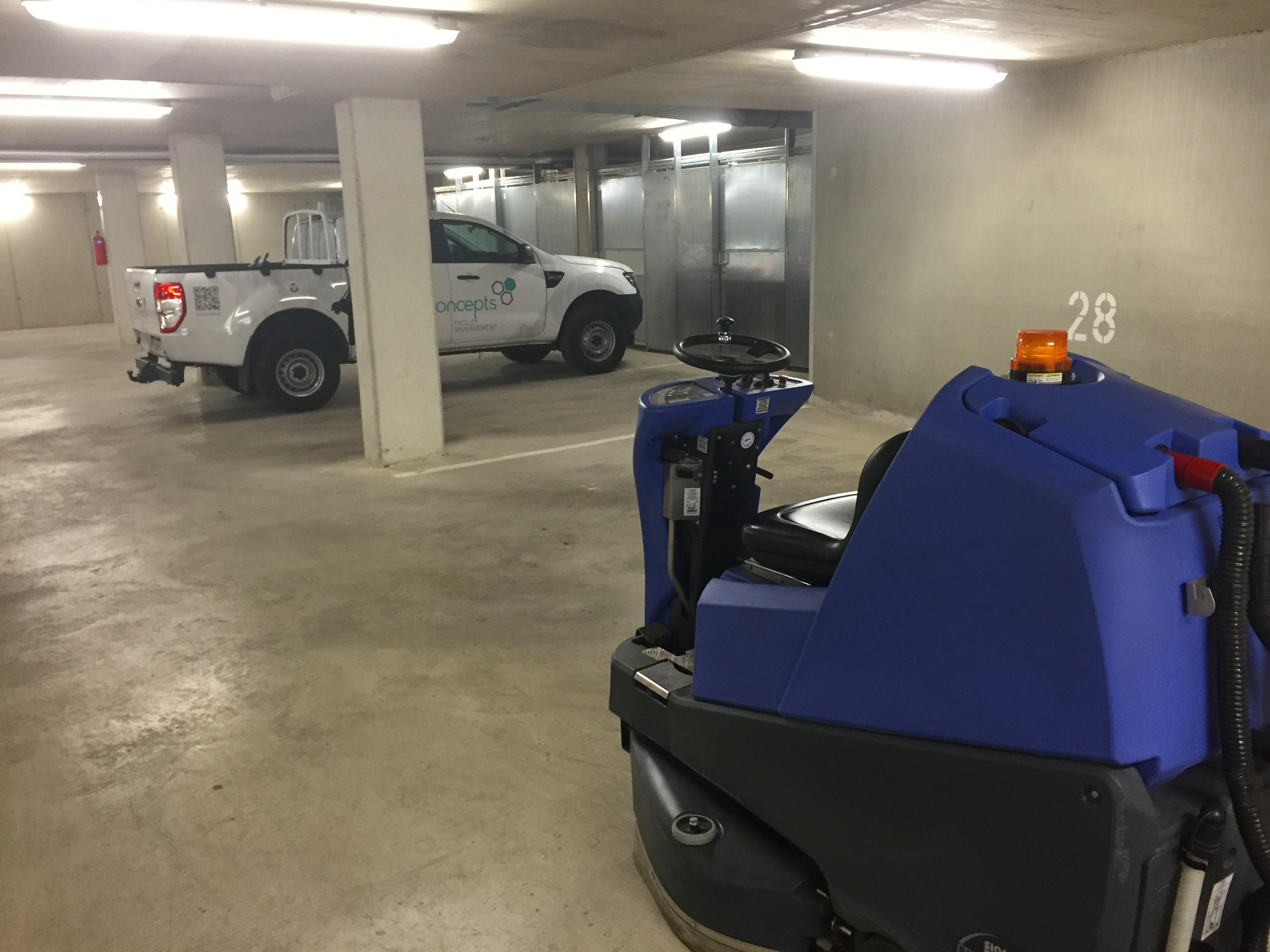 Blaue Reinigungsmaschine in einer Tiefgarage mit einem weißen Fahrzeug im Hintergrund.