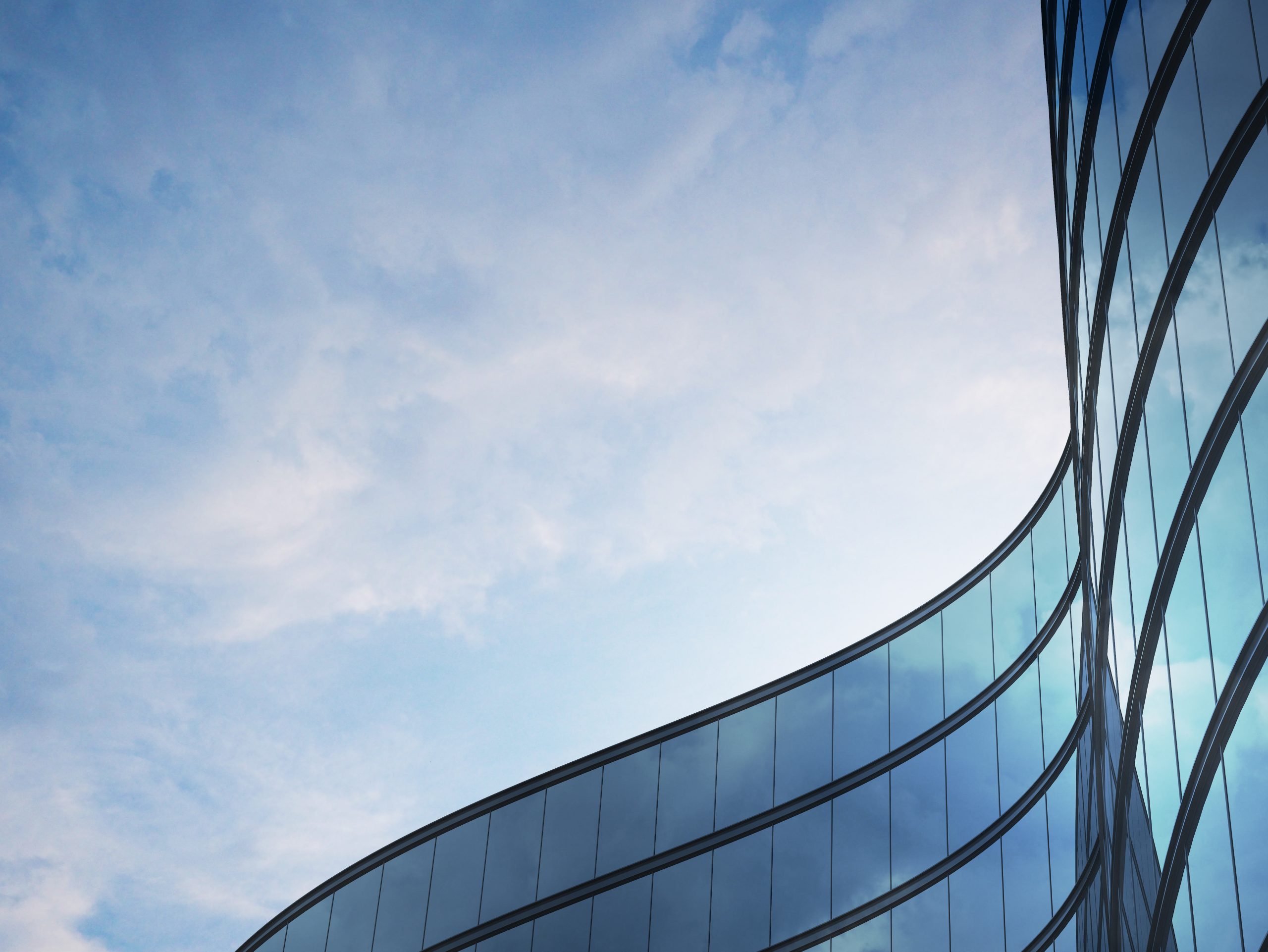 Fassadenansicht eines modernen Bürogebäudes mit geschwungenen Glasfronten, die den blauen Himmel spiegeln.