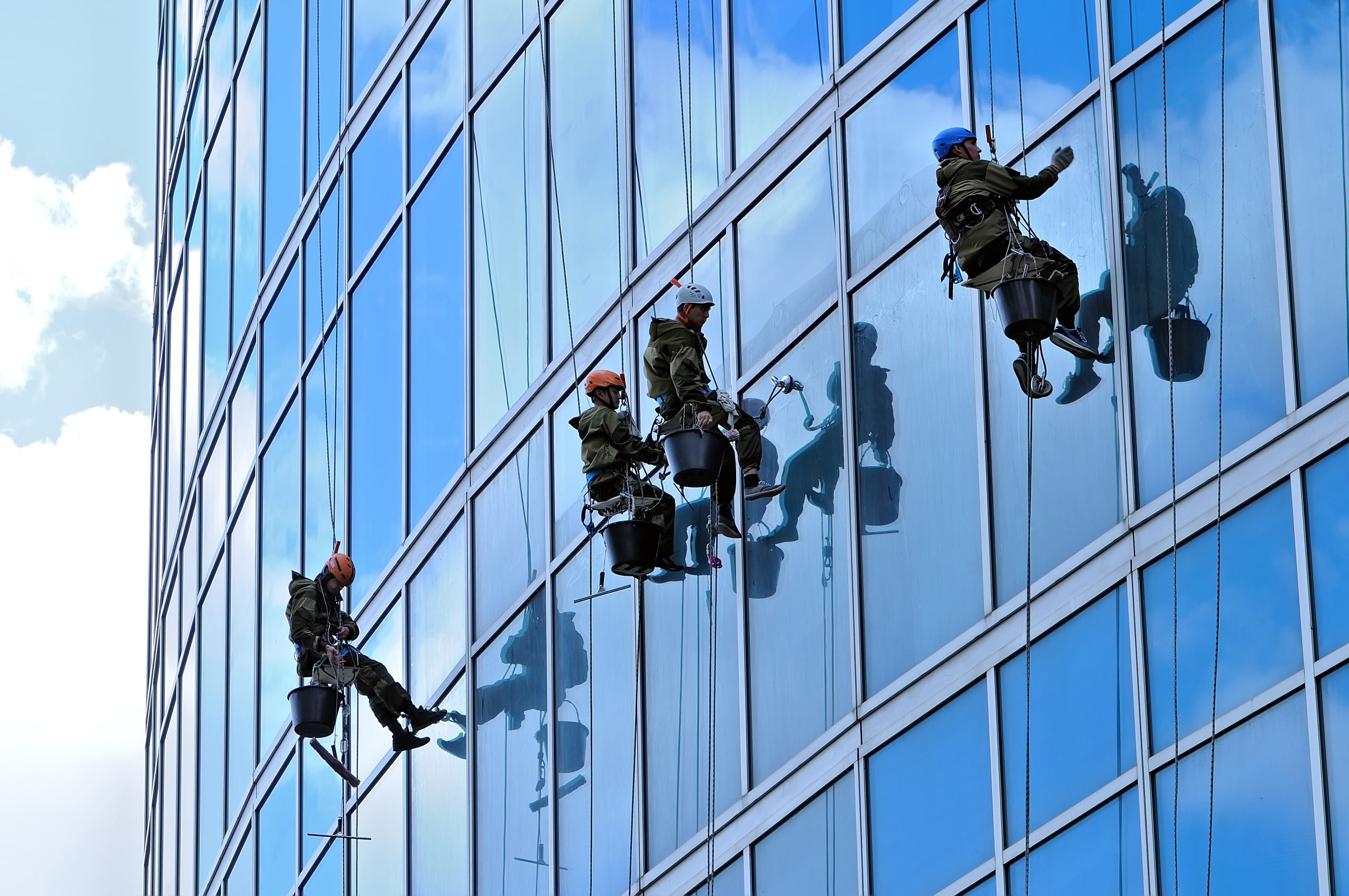 Drei Fensterputzer, die an der Fassade eines Hochhauses arbeiten und reflektierende Fenster reinigen.