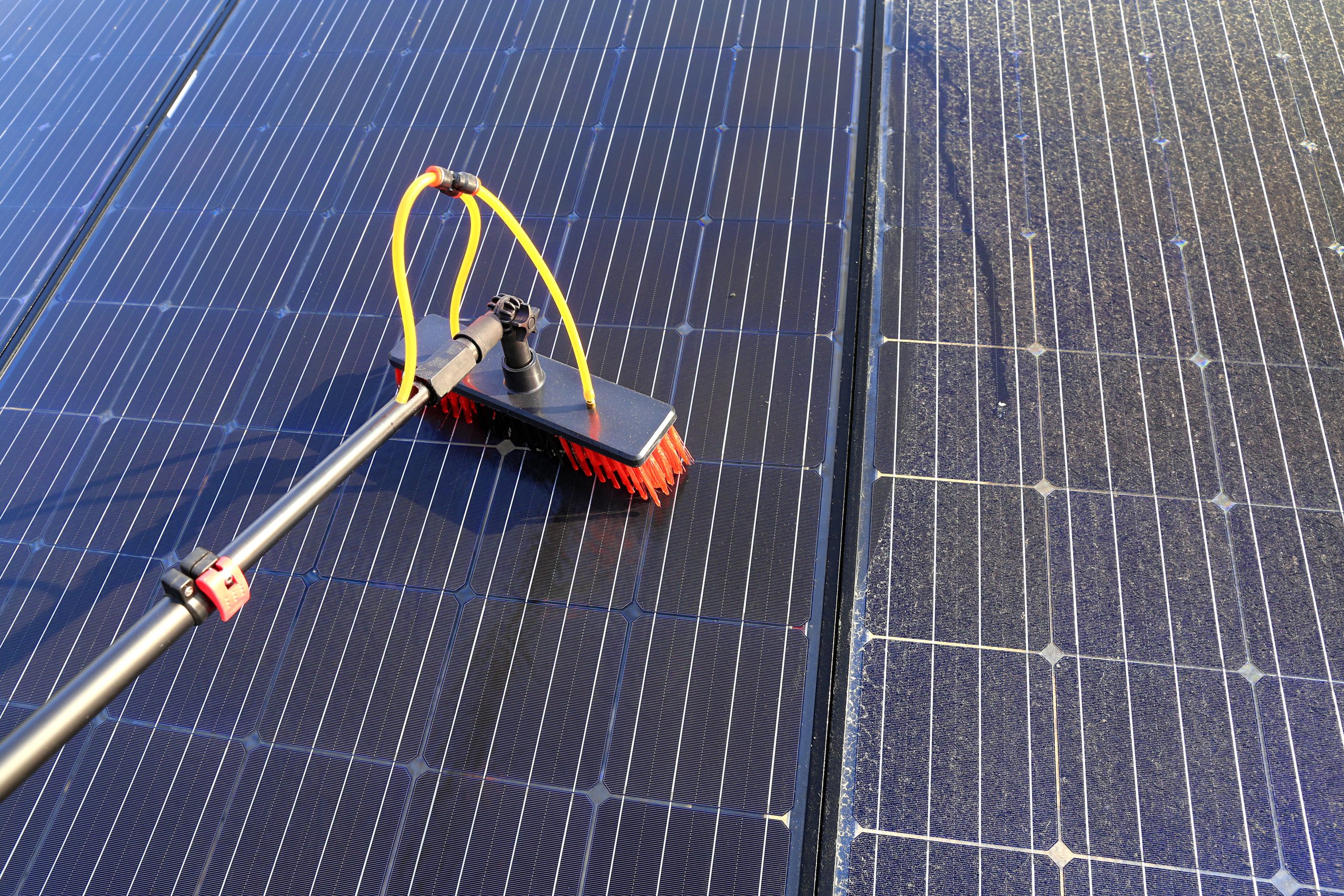 Spezialisierte Bürste mit Wasserdüsen reinigt Solarpanele. Deutlicher Unterschied zwischen gereinigter und verschmutzter Fläche sichtbar.